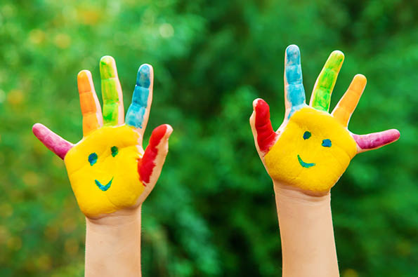 The palms of a child raised up. Palms are painted with smiling faces on them