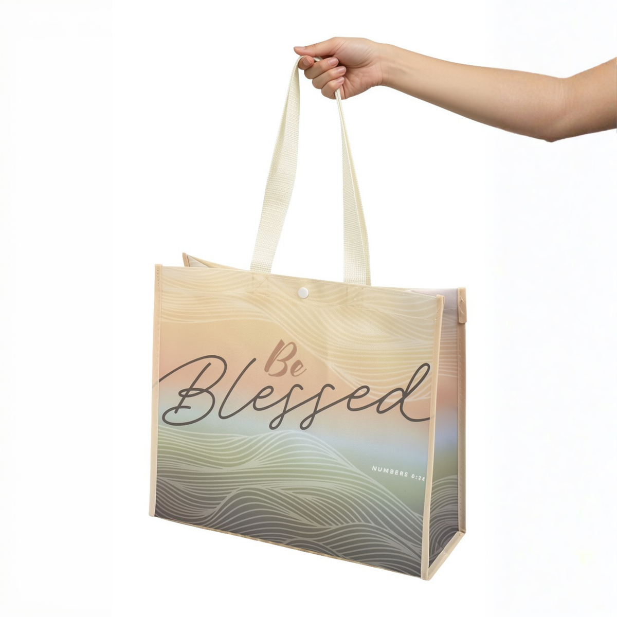 A hand holding a reusable tote bag with cream handles and a beige-to-gray wavy gradient design featuring the words 'Be Blessed' on a white background by CTA Christ to All and CTA Gifts.