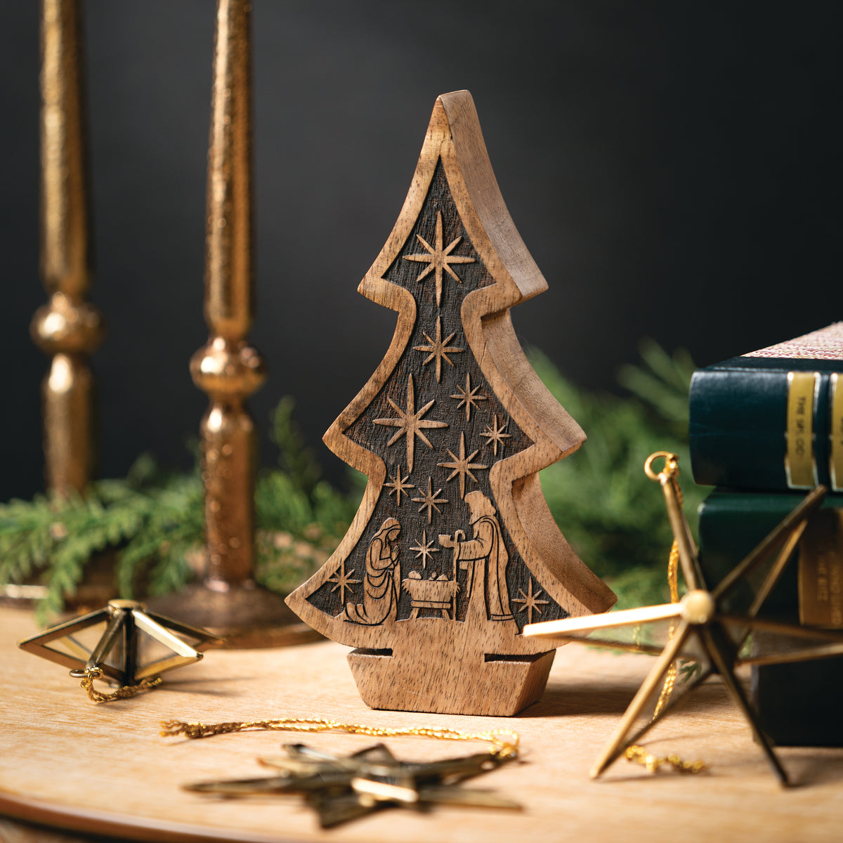 Wooden Christmas tree home decor with nativity scene on a wooden table with candles and greenery.