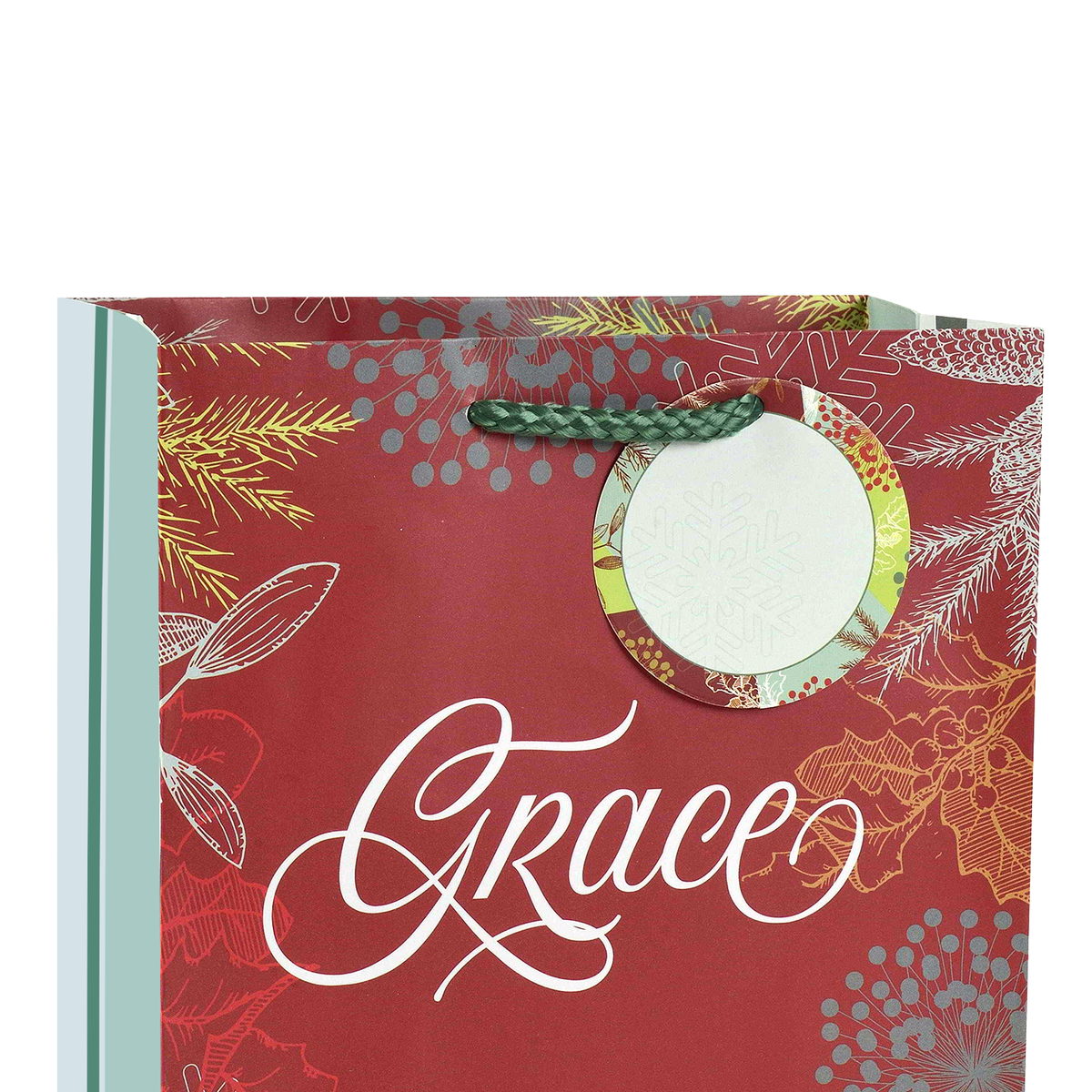 A red holiday-themed paper gift bag with white script text reading 'Grace' and decorative gold, silver, and green floral and berry motifs. A green braided loop handle is attached near the top right, and a circular clear window with patterned trim is visible on the front by CTA Christ to All and CTA Gifts.