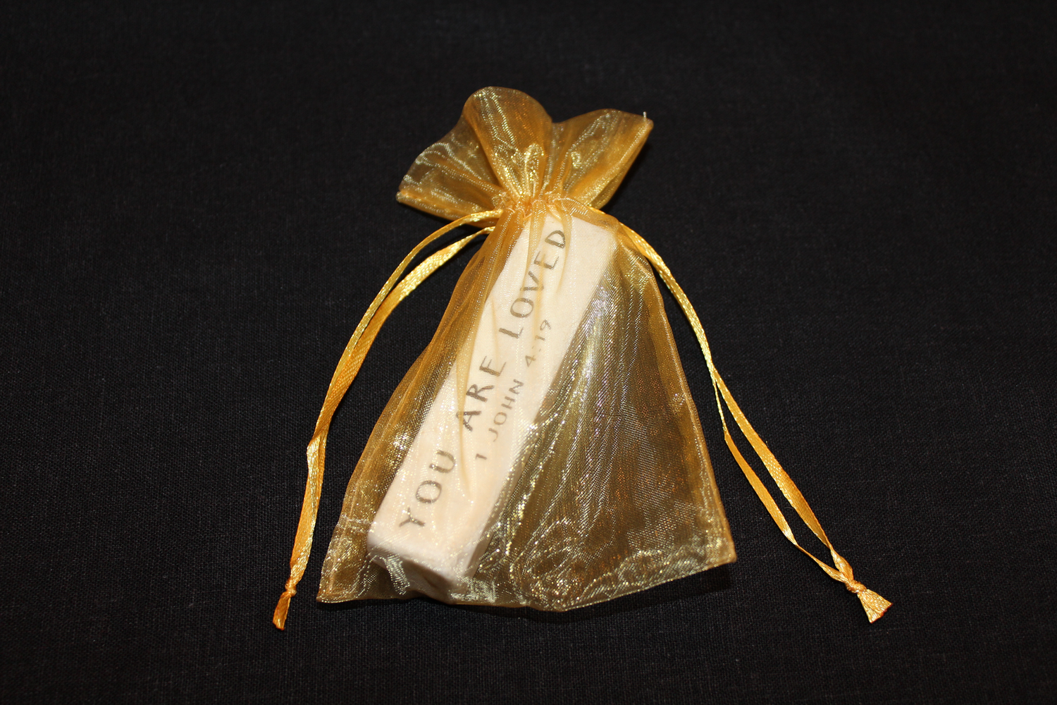 Scripture stone featuring 1 John 4:19 packaged in a gold organza bag