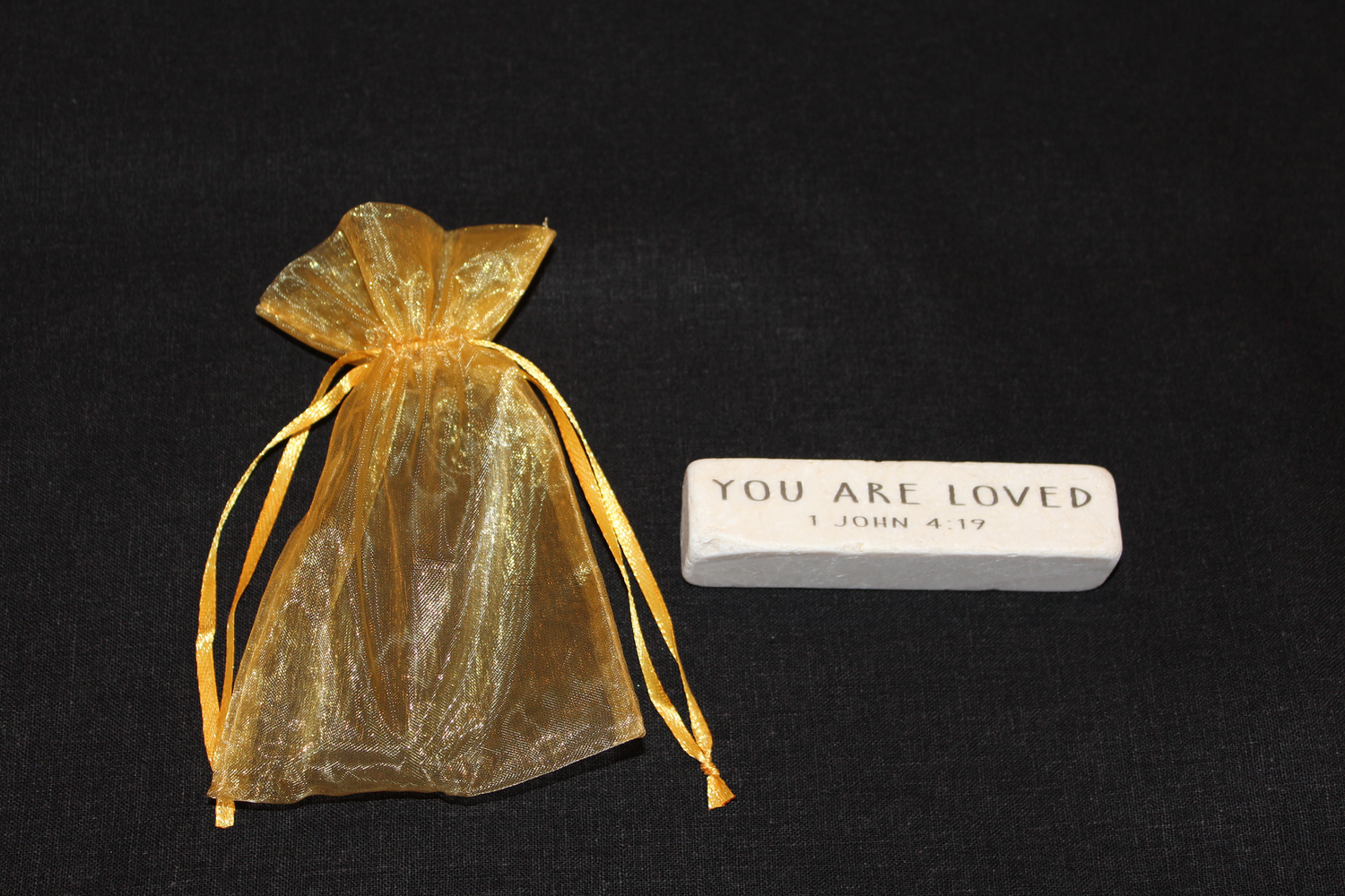 Scripture stone featuring 1 John 4:19 and gold organza bag