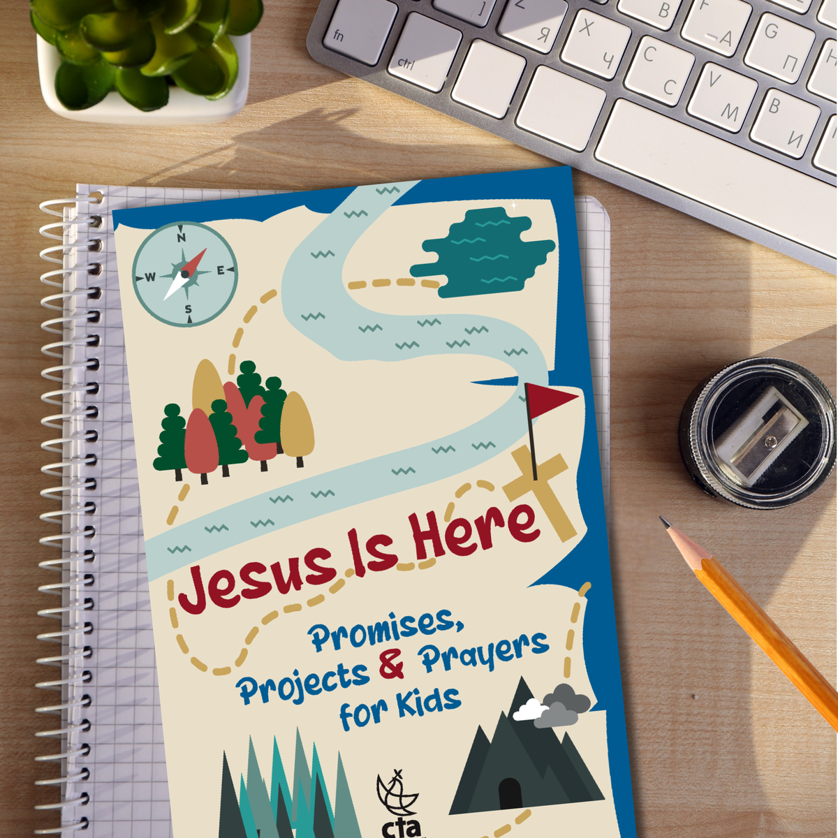 Book titled 'Jesus Is Here: Promises, Projects & Prayers for Kids' on a desk with a keyboard and stationery items by CTA Christ to All and CTAKids.