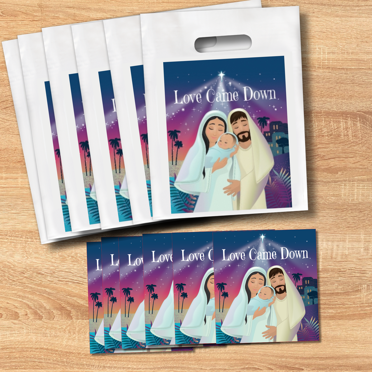 A set of plastic gift bags with a printed Christmas nativity illustration on the front, displayed on a light wood surface. The bags show the text 'Love Came Down' and feature an illustration of Mary, Joseph, and baby Jesus against a purple and blue starry sky with palm trees by CTA Christ to All & CTAKids.