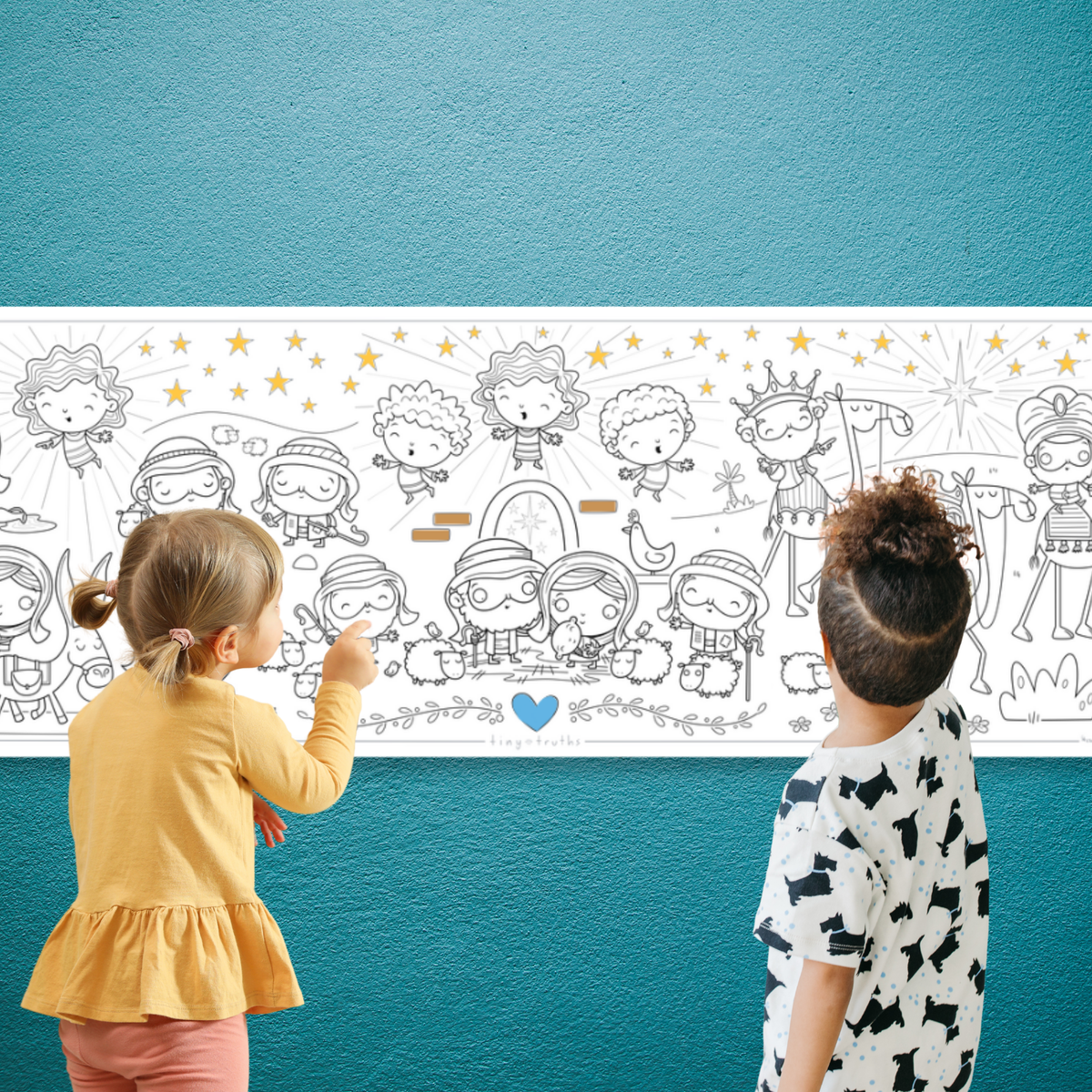 Two children standing in front of a white illustrated border print mounted on a teal wall. The print features black cartoon figures, stars, and small gold details, with a small blue heart near the bottom.