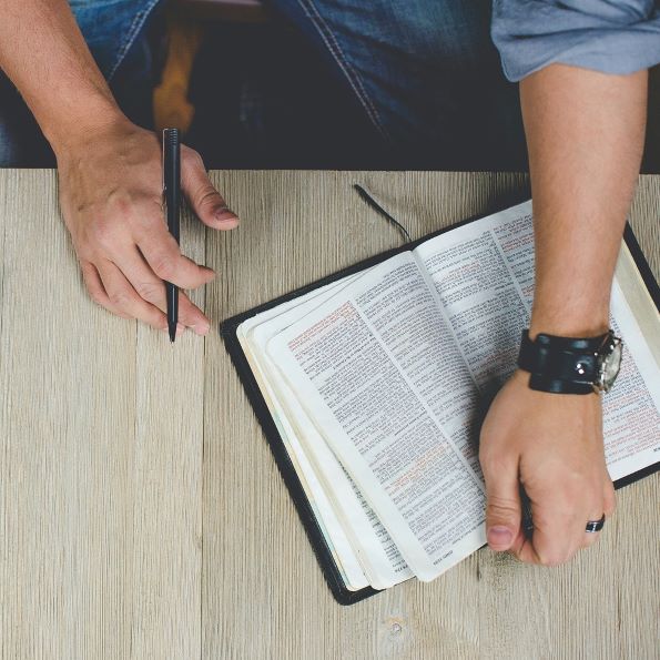 Man with pen in hand and open Bible on desk