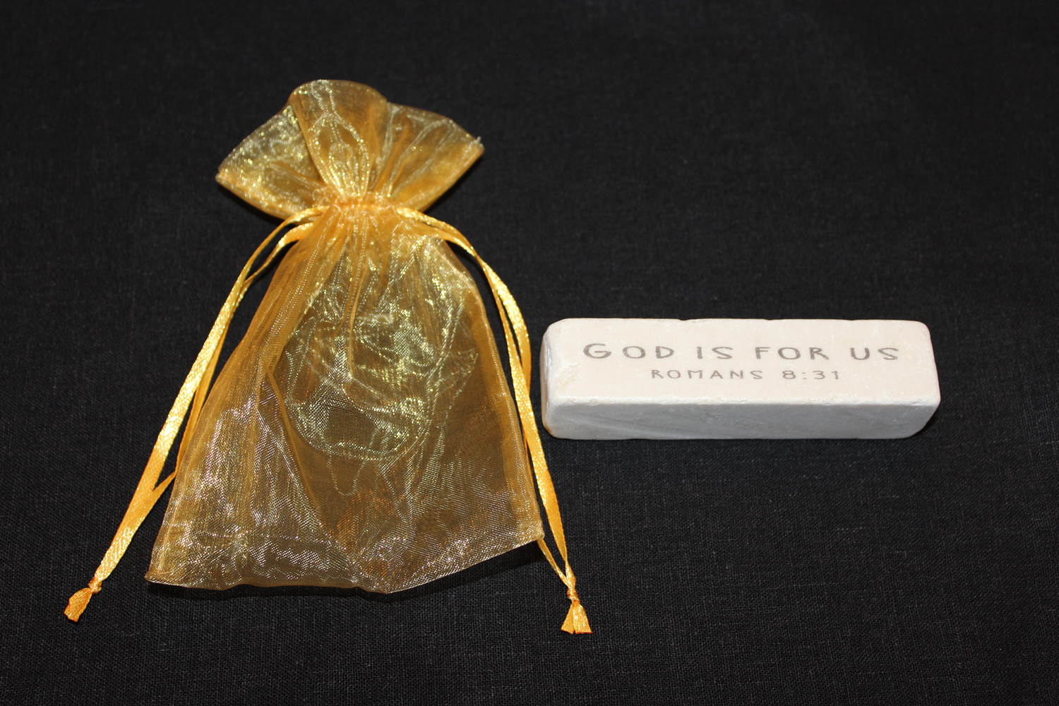 Gold drawstring organza bag next to a white Scripture stone featuring Romans 8:31