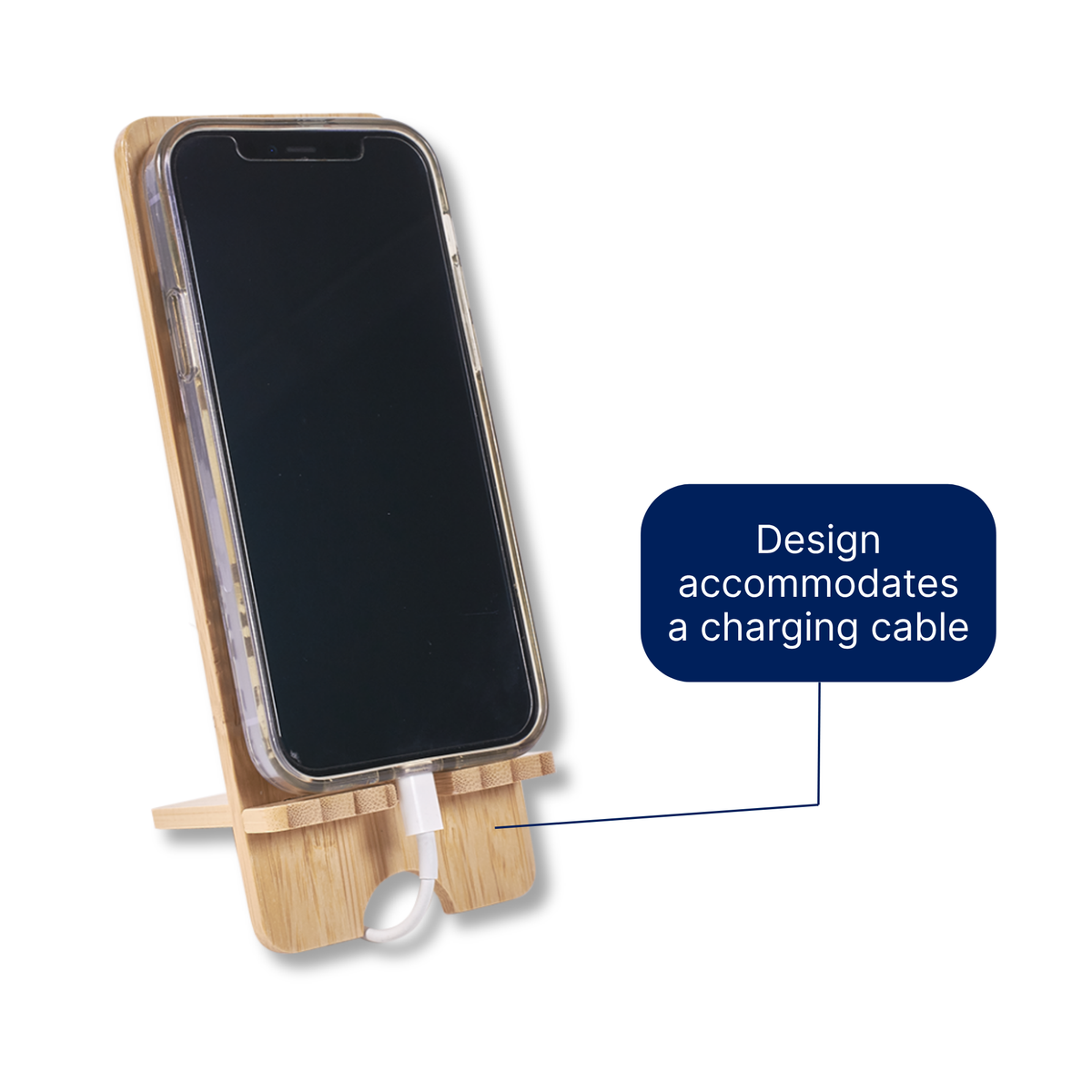 A bamboo phone stand holding a smartphone upright, with a charging cable inserted at the bottom. A blue callout box reads 'Design accommodates a charging cable' on a white background by CTA Christ to All and CTA Gifts.