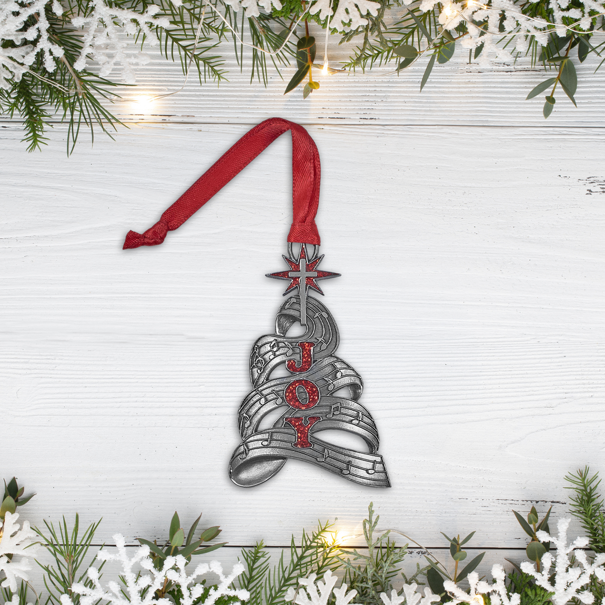 Decorative Christmas bell ornament with 'JOY' on a white wooden background with greenery.