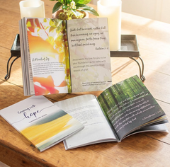 Several copies of Grieving with Hope: Leaning on Jesus are displayed open on a wooden table beside candles and a potted plant. The devotional book includes Scripture passages, reflections, and Christian encouragement for those experiencing grief by CTA Christ to All and CTA Publishing.