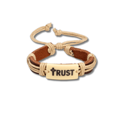 A multi-strand cord bracelet featuring brown leather wrap, beige rope, and a central cream-colored rectangular plate engraved with the word 'TRUST' and a small cross by CTA Christ to All & CTAKids.