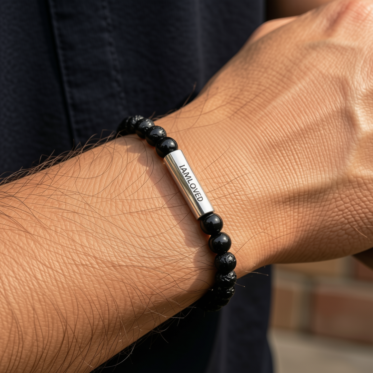 A close-up of a person's wrist wearing a beaded bracelet with black round beads and a central silver-toned metal cylinder engraved with 'I AM LOVER' by CTA Christ to All & CTA Gifts.