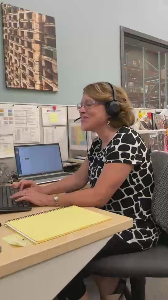 Friendly phone conversation with a Customer Service Representative at CTA Christ to All.  She's smiling and typing away happily in an office/warehouse environment while speaking with a customer on the phone.